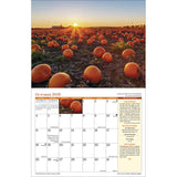 the interior page of the 2026 Country calendar open to the October page featuring a photo of a pumpkin field as the sun sets over the farm