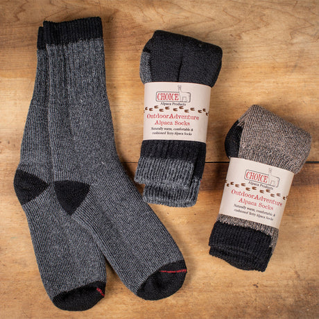 3 pairs of alpaca outdoor adventure socks - the gray pair is laid flat showing the detail of the sock and is next to a packaged black pair and a packaged cocoa brown pair