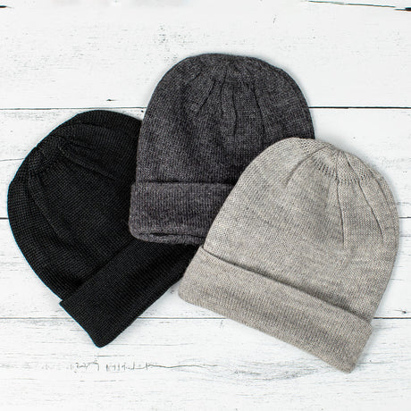 a trio of alpaca hats fanned on a white wood background - colors pictured are black, gray, and silver