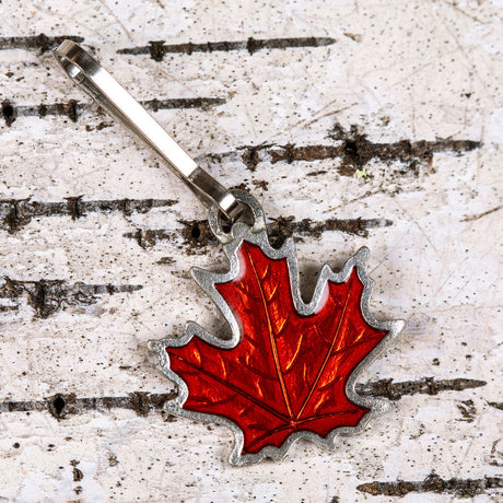a handcrafted pewter and rust orange colored maple leaf zipper pull on a birch bark background
