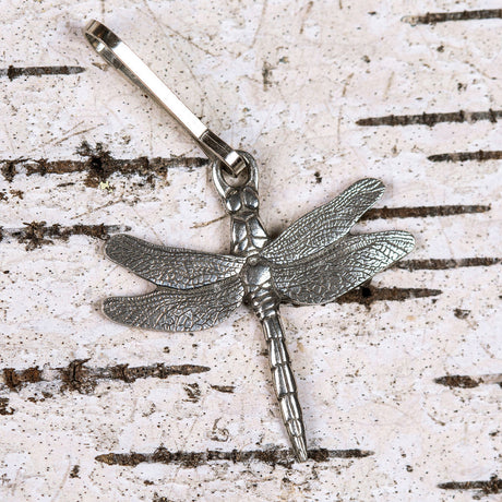 a highly detailed pewter dragonfly zipper pull laid against white birch bark