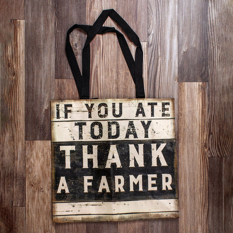 a square woven nylon market tote with wooden plank print and a graphic of black and white painted sign that reads "if you ate today thank a farmer"