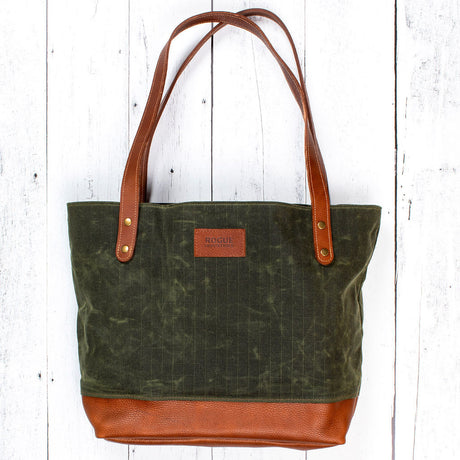 a forest green waxed canvas tote bag with copper leather gusset and handles laid flat on a white wood floor