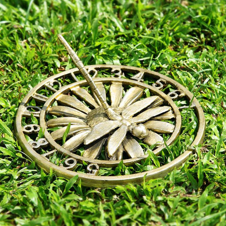 On a lawn sits a sundial of a dragonfly resting on a flower