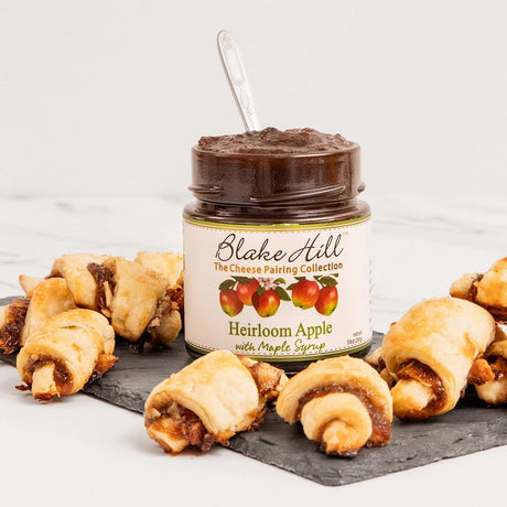 an open jar of the Heirloom Apple with Maple butter on a serving tray next to some rolled pastries that are filled with the apple with maple butter.