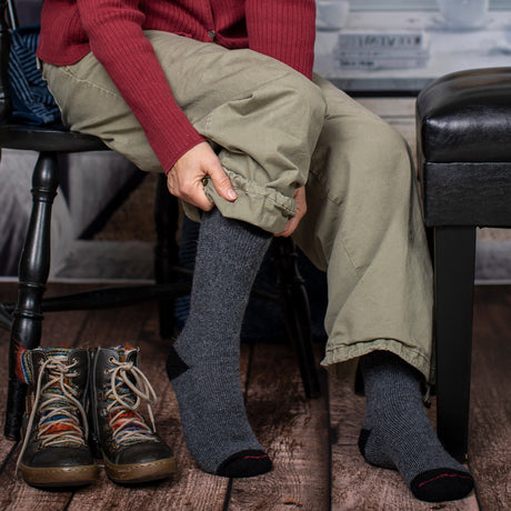 medium view of a model sitting in a chair pulling on her gray alpaca socks