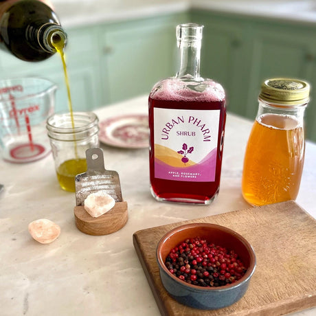 a kitchen counter with a bottle of Apple Rosemary shrub and fresh ingredients