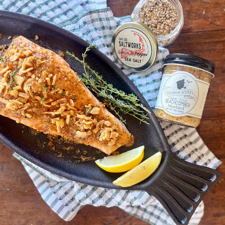 a tabletop with a jar of Beachcomber Mustard alongside a filet of fish garnished with herbs and lemon