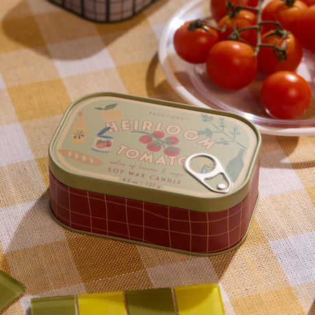 Small tin can with 'Heirloom Tomato' design on a checkered tablecloth with tomatoes in the background.