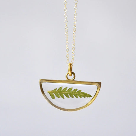 a gold half moon shaped clear resin pendant necklace with real pressed fern inside and outlined in gold, hanging from a gold chain