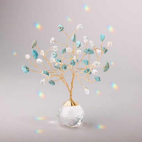 Decorative tree with gold branches and crystal base adorned with turquoise and clear crystals casting tiny rainbows against the light gray background