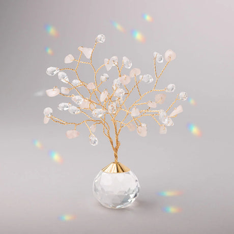 Decorative tree with gold branches and crystal base adorned with rose quartz and clear crystals casting tiny rainbows against the light gray background