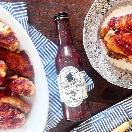 cranberry lime hot sauce bottle on a table laying between two plates of food
