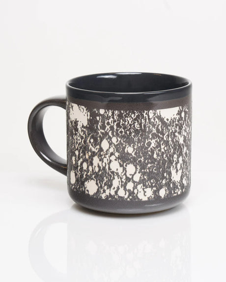 a gray ceramic mug with wrap around carved details of the surface of the moon in white