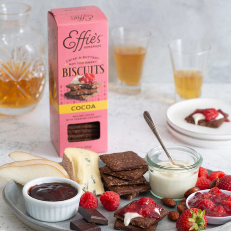a delicious snack spread on a white table featuring Effie's Cocoa biscuits alongside a tray of treats including berries, cream, cheese, and chocolate