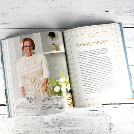Open book showing a recipe for 'Sunday Suppers' with a woman in an apron on a wooden surface.