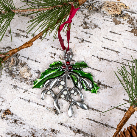 the mistletoe ornament laid on a white birch bark background with its red satin ribbon fixed to evergreen boughs