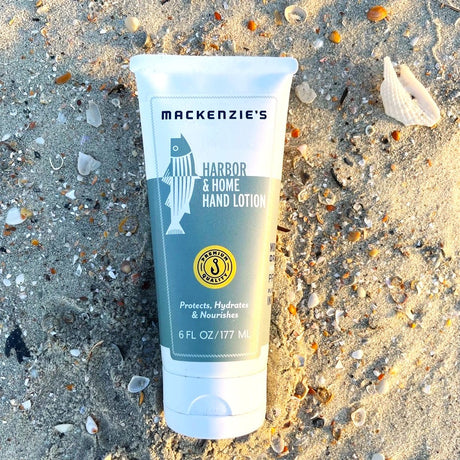 a bottle of the Harbor and Home Hand lotion with white and sea green label on a sandy beach