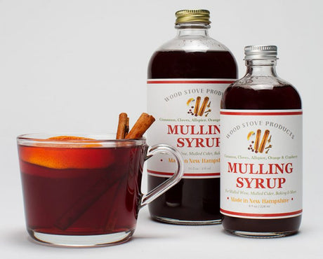 two bottles of mulling syrup next to a clear glass mug filled with a mulled beverage and two cinnamon sticks