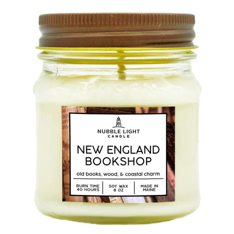 a candle in a clear glass mason jar with off white wax and a label that reads "New England Bookshop" against a white background