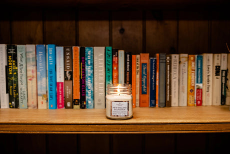 a bookshelf filled with books and a New England Bookshop candle burning on the shelf