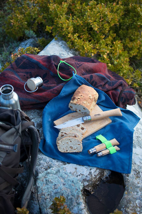 the Nomad Cooking kit with a loaf of bread on the cutting board laid out on a rock alongside other camping gear