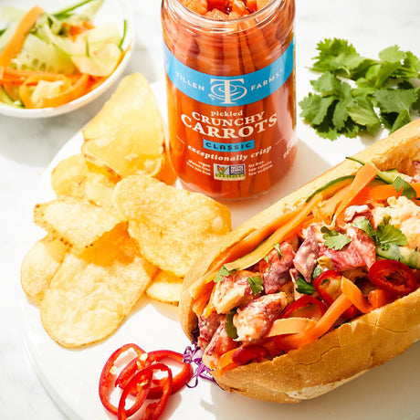 a tasty looking sandwich spread alongside a jar of pickled crunchy carrots