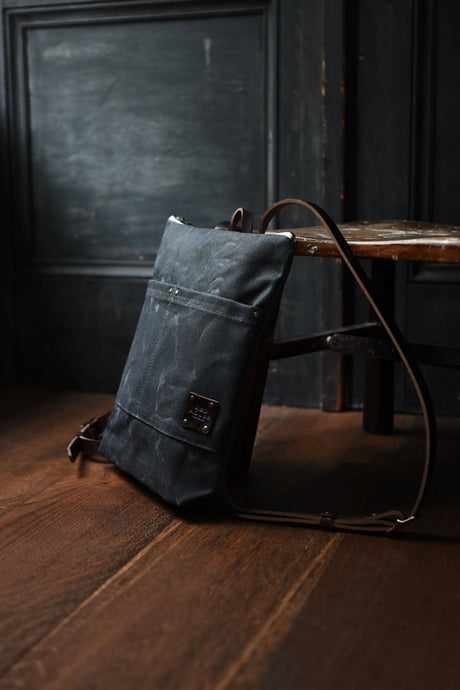 the Day Pack in Ash rests against a chair in a dark rustic room