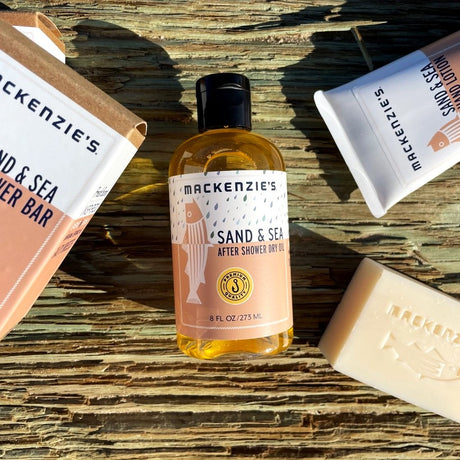 the Sand and Sea Sampler products spread on a wooden dock with the Sand and Sea After Shower Dry Oil in the center