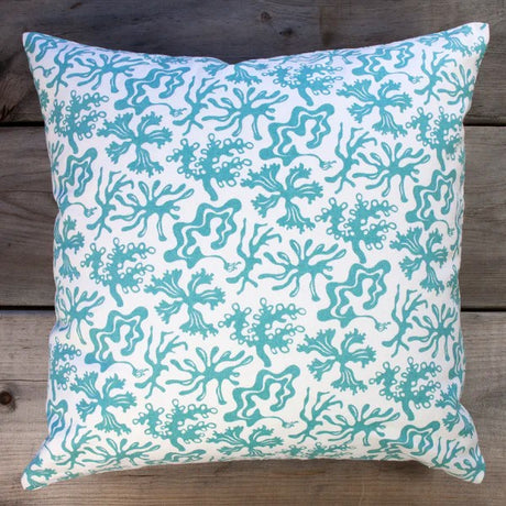 Decorative pillow with teal seaweed pattern on a wooden surface