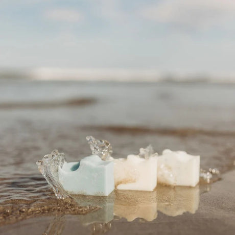 the sel de mer soap trio on the seashore with a small wave splashing against the bars of soap
