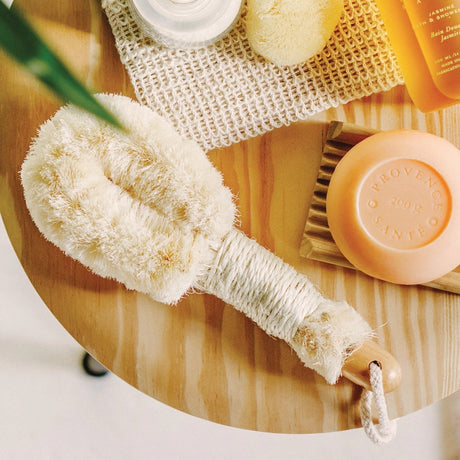 a spa view of the sisal brush on a bamboo platter next to a bar of soap and other bath tools showing the brush as an essential part of your self care routine