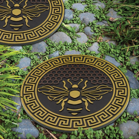 two garden stepping stones with bee design and honeycomb background installed in a stony garden pathway 