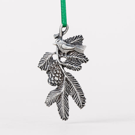 A delicately detailed handcrafted pewter ornament of a bird on a pine bough with a green silk ribbon