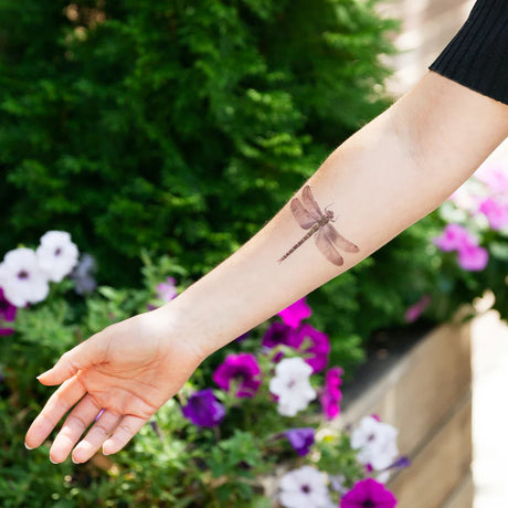 in a lush garden is a model's arm with the dragonfly tattoo applied to the inner forearm