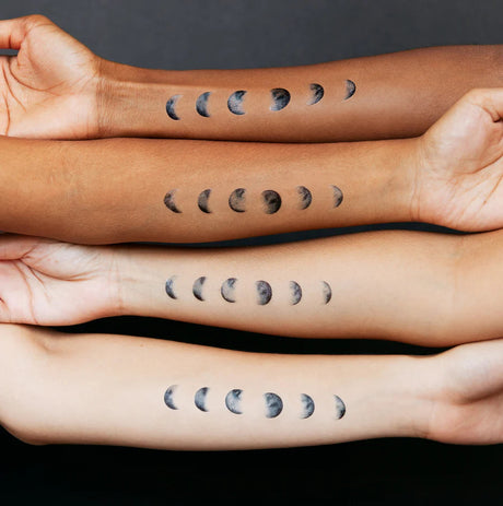 four arms of varying skin tones with the moon phase tattoos applied to their skin to show how the tattoos appear on various skin tones