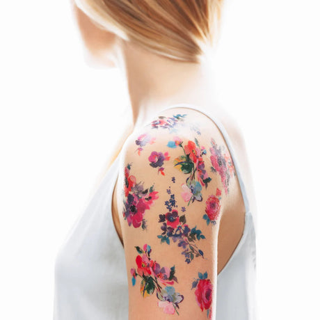 profile view of a model's upper arm showing multiple watercolor floral tattoos applied on their arm