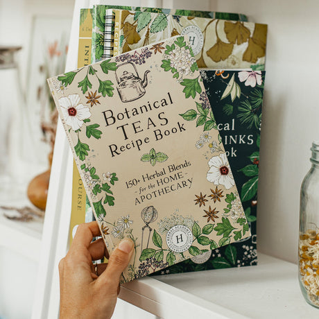 The Botanical Teas Recipe Book being taken off a bookshelf with other botanical themed books