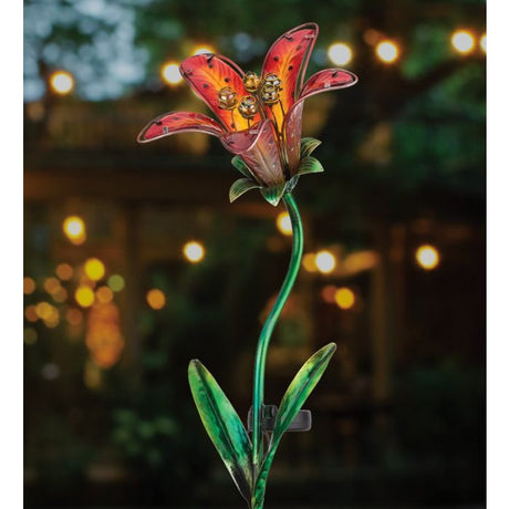 the red tiger lily solar stake illuminated in a garden at night