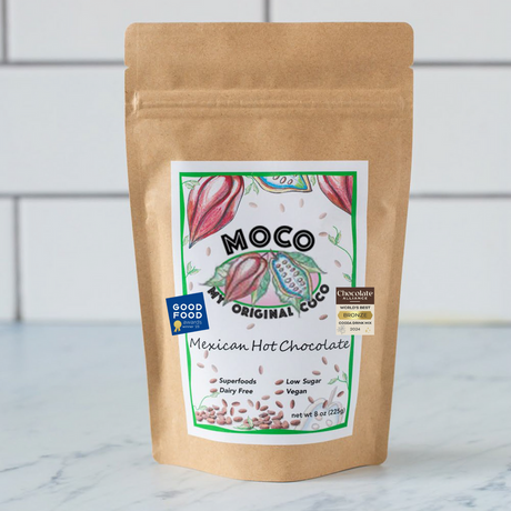 a kraft hot cocoa package with a white label with red and green illustrations of cocoa beans that reads "MOCO My Original Coco - Mexican Hot Chocolate"