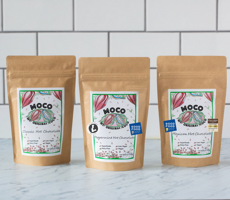 a trio of hot cocoa packages against a white tile background