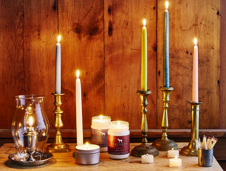 a tabletop filled with various candlesticks, oil lamps, tea light candles, and jar candles all giving off a warm glow